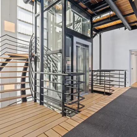 Modern office interior at Maanlander 43, Amersfoort Calveen with sleek elevator, spiral staircase, and wooden flooring. Ideal office space rental opportunity.
