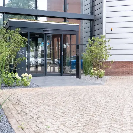 Entrance to the modern office building at Maanlander 43, Amersfoort Calveen, featuring glass doors and surrounding greenery.