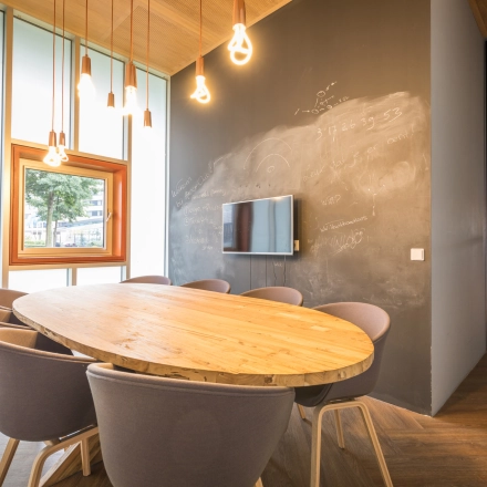 Modern conference room at Maanlander 47, Amersfoort Calveen, suitable for office space rental, featuring a wooden table, chairs, chalkboard wall, and pendant lights.