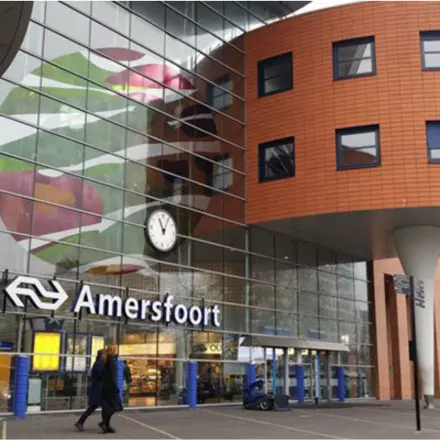 Exterior view of Amersfoort Centraal Station with modern design elements and people walking by.
