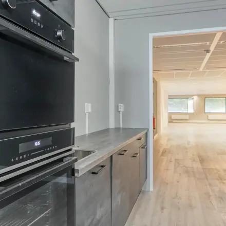 View of an office space rental in Amersfoort Centrum featuring a small kitchen area leading to an open workspace with large windows.