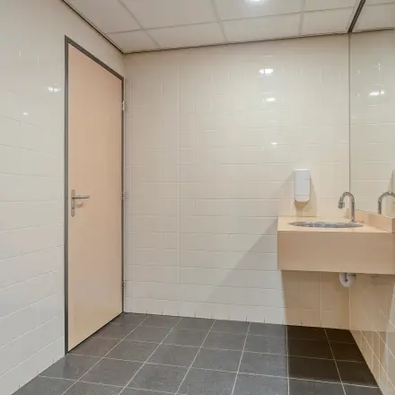 Office restroom with tiled walls, a wooden door, and a sink located at Asch van Wijckstraat 2-4 in Amersfoort Centrum, suitable for office space rental.