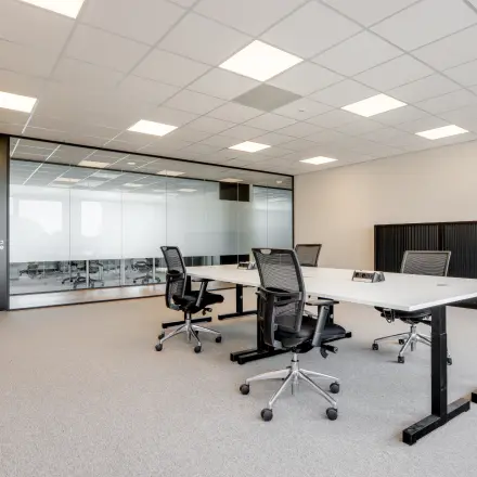 Furnished office space for rent at De Gondel 1, Amstelveen, featuring modern desks and chairs in a bright, carpeted room with glass partitions.