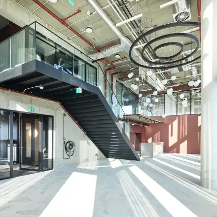 Modern office space with high ceilings and industrial design in Amsterdam Amstel Business Park, featuring large windows and a striking staircase, ideal for office space rental.
