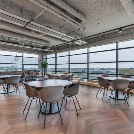 Bright and spacious furnished office interior with round tables and chairs, offering a view over Amsterdam Amstel Business Park, ideal for office space rental.