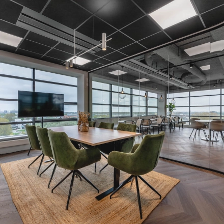 Spacious office space at Joop Geesinkweg 201 featuring large windows, green chairs, and glass partitions. Ideal for office space rental in Amsterdam Amstel Business Park.