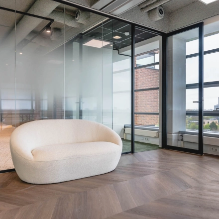 Modern office space at Joop Geesinkweg 201, featuring a sleek interior with glass walls and a stylish sofa, ideal for rent at Amsterdam Amstel Business Park.