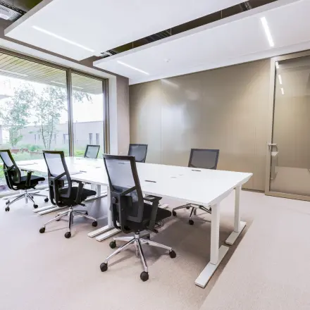 Modern office space rental in Amsterdam Amstel with a large table and chairs, featuring glass walls and natural light.