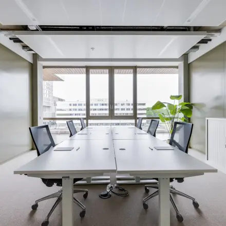 Modern office space in Amsterdam Amstel with large windows, conference tables, and sleek chairs. Ideal for office space rental.