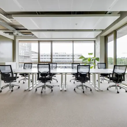 Bright office space with large windows and several desks and chairs, offering a professional workspace for rent in Amsterdam Amstel.