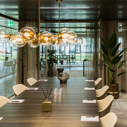 Spacious meeting room at Walborg 2A in Amsterdam Buitenveldert, ideal for office space rental, with a long table, modern lighting, and curtains framing glass walls.