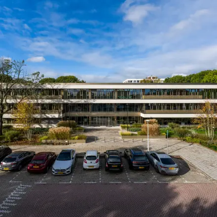 Exterior view of the office building at Walborg 2A in Amsterdam Buitenveldert, featuring ample parking space and surrounded by greenery, ideal for office space rental.