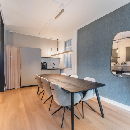 Interior view of a furnished office space rental on Herengracht 221, Amsterdam Canal Belt, featuring a conference table with chairs and a kitchenette.