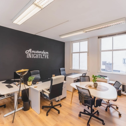 Bright, furnished office space for rent at Herengracht 221, Amsterdam Canal Belt, featuring modern desks and chairs with natural light from large windows.