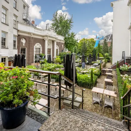 Charming outdoor area at Herengracht 459-469 in the Amsterdam Canal Belt, featuring a patio with tables and lush greenery, ideal for office space rental.
