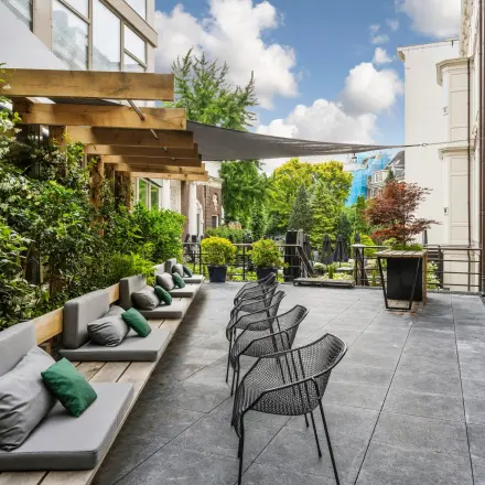 Outdoor seating area at Herengracht 459-469, ideal for office space rental with a mix of comfortable benches and modern chairs amid lush greenery.