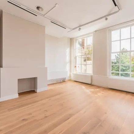 Bright, unfurnished office space with wooden flooring and large windows overlooking the Amsterdam Canal Belt, ideal for office space rental.