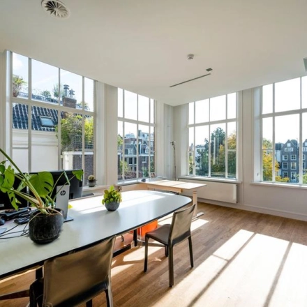 Bright office space rental in Amsterdam Canal Belt at Herengracht 582-584 with large windows, plants, and modern furniture.