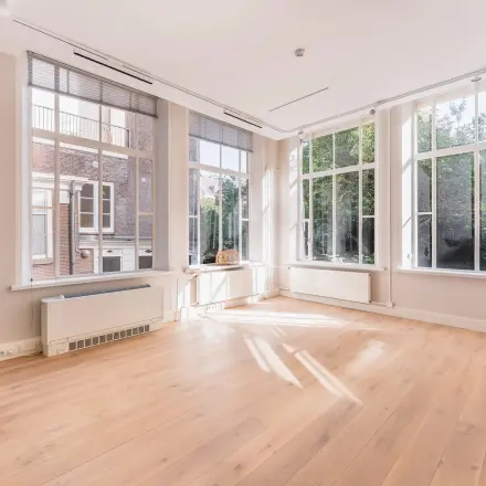 Bright, unfurnished office space available for rent at Herengracht 582-584 in Amsterdam Canal Belt, featuring large windows with garden views and wooden flooring.