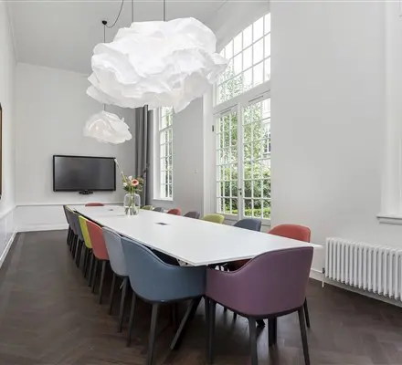 Bright, modern office space rental in Amsterdam Canal Belt, featuring a long table with colorful chairs under unique pendant lights, perfect for meetings.