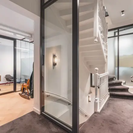 Bright office space in Amsterdam Center with modern glass partitions and sleek design, ideal for rent. Features a staircase and furnished areas for effective office space rental.