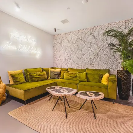Cozy office lounge area at Hekelveld 8-10, Amsterdam Center, featuring green velvet sofa, decorative wall art, and elegant coffee tables.