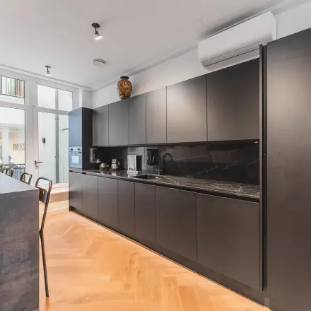 Modern kitchen area in an Amsterdam office with sleek black cabinetry, bar seating, and natural lighting, perfect for office space rental.