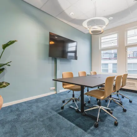 Bright office space with a meeting table, chairs, and a wall-mounted TV at Herengracht 471, perfect for office space rental in Amsterdam Center.
