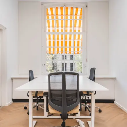 Bright office space with desks and chairs, located at Herengracht 471, Amsterdam Center, available for rent. Ideal for small teams.