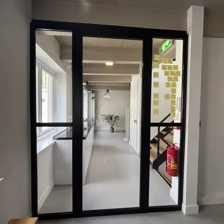 A modern office space to rent at Kloveniersburgwal 131K, Amsterdam Center. The interior is furnished with a sleek glass door, natural light, and contemporary design elements.
