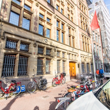 Exterior view of an office building located at Nieuwezijds Voorburgwal 104-108 in Amsterdam Center, featuring bicycles parked along the sidewalk and people walking by.
