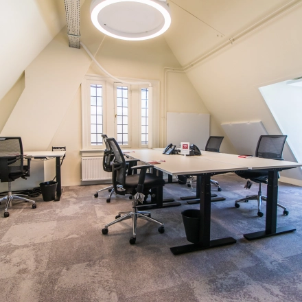 Bright office space for rent in Amsterdam Center, showcasing a furnished area with desks and chairs under a unique circular light fixture.