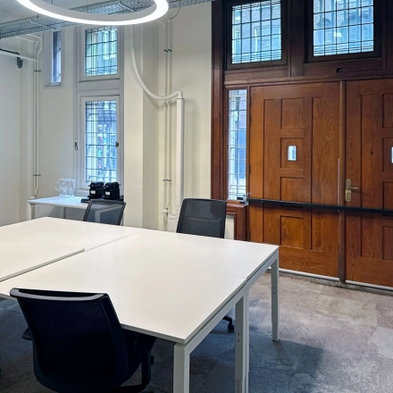 Interior view of an Amsterdam office space with modern desks and chairs near a wooden door, available for rent at Nieuwezijds Voorburgwal 104-108.