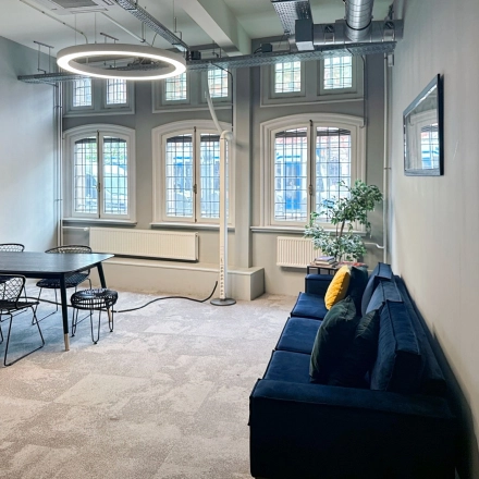 Bright office space in Amsterdam Center with modern furnishings, featuring a large table and seating area under stylish lighting. Perfect for office space rental on Nieuwezijds Voorburgwal.