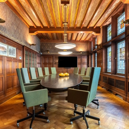 Charming conference room with wood paneling, featuring a large oval table surrounded by green upholstered chairs, ideal for office space rental in Amsterdam Center.