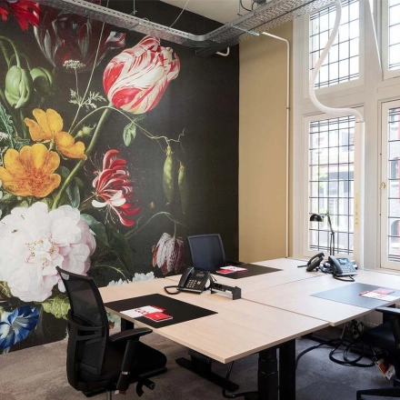 Bright office space at Nieuwezijds Voorburgwal 104-108, Amsterdam Center, featuring a bold floral mural and well-lit workstations for rent.