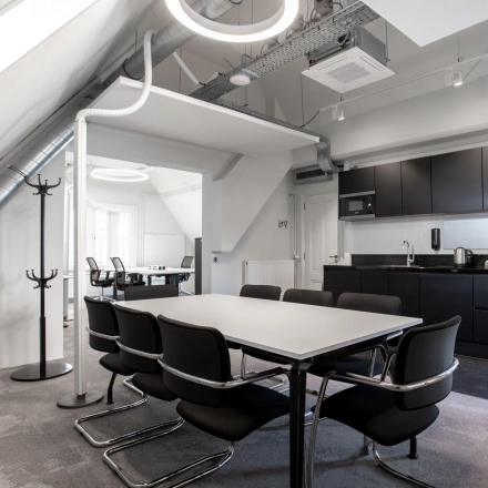 Modern office to rent at Nieuwezijds Voorburgwal 104-108, Amsterdam Center, featuring a sleek meeting table, black chairs, and a kitchenette. Ideal for collaborative work and meetings.