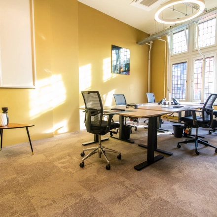 Bright office space with four workstations, modern chairs, and a small side table near large windows at Nieuwezijds Voorburgwal 104-108, ideal for office space rental in Amsterdam Center.