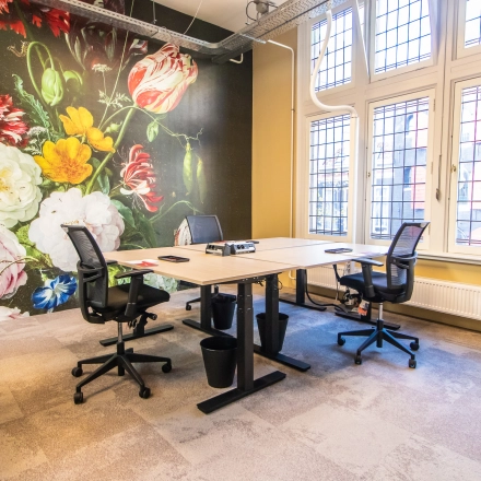 Bright office space for rent in Amsterdam Center, featuring modern furnishings and large windows. Ideal for business activities against a vibrant floral mural.