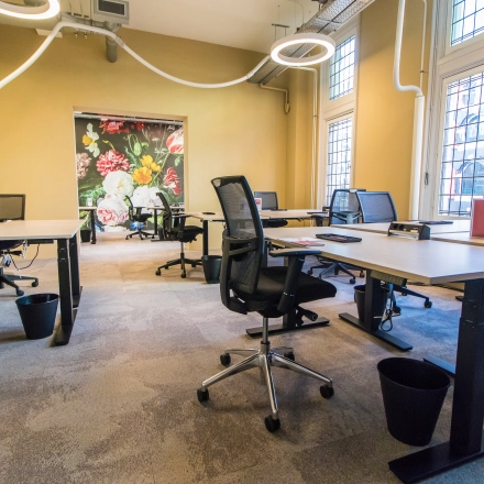 Bright office space with modern workstations and charming floral wall art, available for rent at Nieuwezijds Voorburgwal 104-108, Amsterdam Center. Perfect for dynamic and creative professionals seeking office space rental.