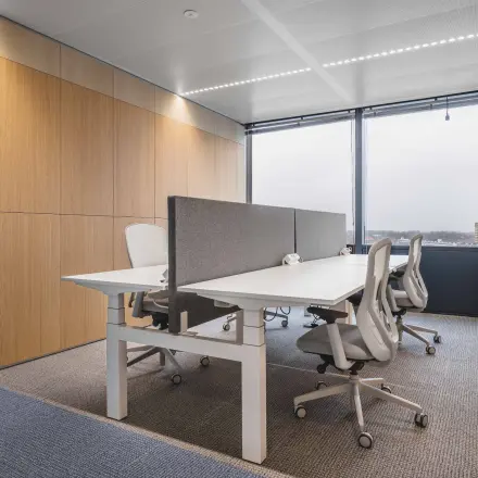 Furnished office space at Piet Heinkade 55, Amsterdam Center, featuring modern workstations with ergonomic chairs and a view through large windows.