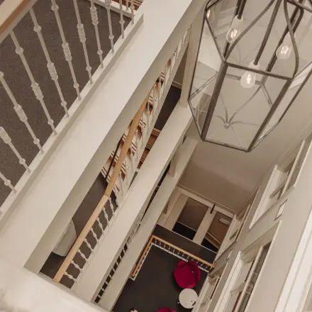 Interior view of an office space rental at Prins Hendrikkade 14, Amsterdam Center, featuring a multi-story staircase with modern lighting and seating area with pink chairs.