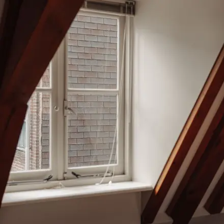 Interior view of office with a slanted ceiling and a window at Prins Hendrikkade 14, Amsterdam Center, ideal for those seeking office space rental with character.