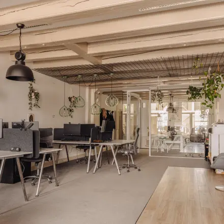 Modern office space at Prins Hendrikkade 14, Amsterdam Center, featuring open desks with computers, chairs, and decorative plants, ideal for office space rental.