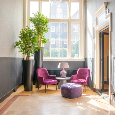Bright office lounge at Raamplein 1, Amsterdam Center with vibrant purple chairs and a window view, perfect for office space rental.