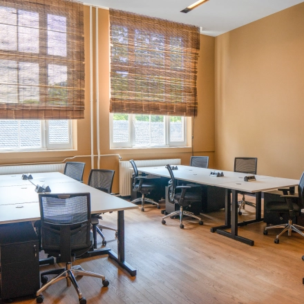 Bright office space with multiple desks and chairs, large windows with blinds, located at Raamplein 1 in Amsterdam Center. Ideal for office space rental.
