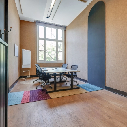 Interior view of a furnished office to rent at Raamplein 1, Amsterdam Center, featuring a meeting table with chairs and a large window.