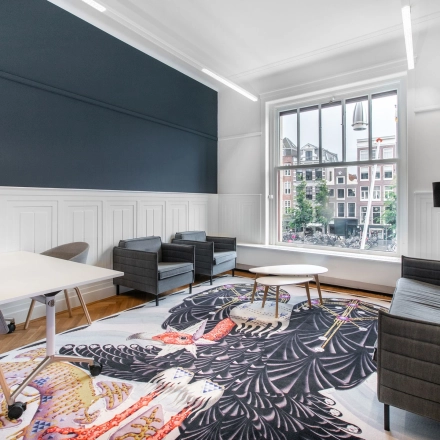Modern office space rental at Rokin 92-96, Amsterdam Center, featuring contemporary furnishings with a vibrant rug and city views. Ideal office to rent for creative professionals.
