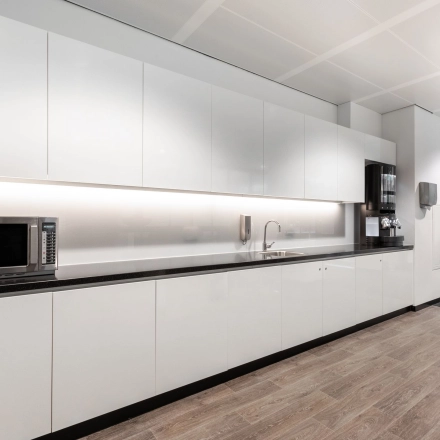 Modern office kitchen area at Rokin 92-96, Amsterdam Center, ideal for office space rental, featuring sleek white cabinets, a microwave, and a coffee machine.