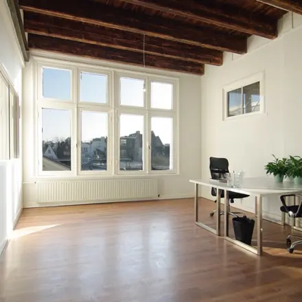 Bright office space with two desks and chairs at Warmoesstraat 155, Amsterdam Center, featuring large windows and wooden floors, ideal for rent office space. The room is empty and ready for use.